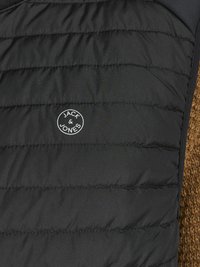 Crna pufasta prsluk s prešanim uzorkom, s jedne strane od smešnog flisa. Logotip "JACK & JONES" u bijeloj boji na prednjoj strani.