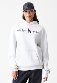 Moleton cinza claro feito de tecido macio, com o texto bordado "Los Angeles Dodgers" e um bolso frontal. Combinado com um boné preto elegante.