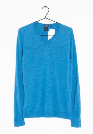 Suéter azul de manga larga con cuello en V colgado en una percha negra, con etiqueta de marca visible y etiqueta de precio blanca sobre fondo blanco liso.