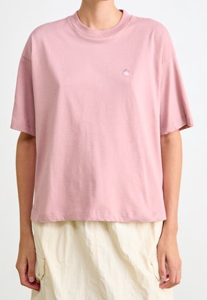 Person wearing a loose light pink short-sleeve t-shirt with a small chest logo and off-white skirt with front pockets.