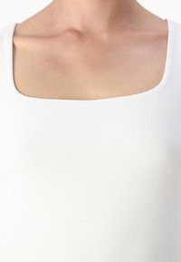 Hvit tettsittende topp med firkantet utringning, glatt tekstur og elastisk materiale, som fremhever et rent, minimalistisk design.