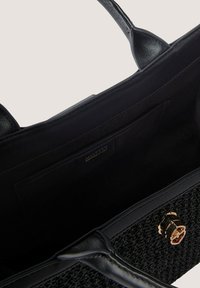Black woven handbag with textured fabric, leather accents, gold hardware, and a spacious interior. Features a zippered pocket and tag.