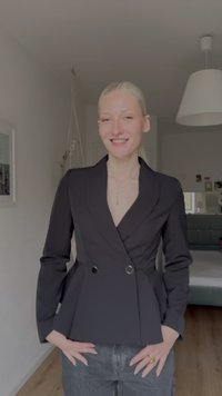 Fekete szabott blézer mély V-nyakkivágással, dupla gombos záródással és peplum derékkal, hosszú ujjakkal és sima textúrával.