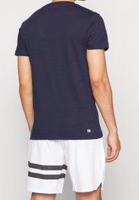 Mörkblå bomullströja med korta ärmar, rund halsringning och liten logotypdetalj vid nederkanten, tillsammans med vita shorts med mörka ränder.