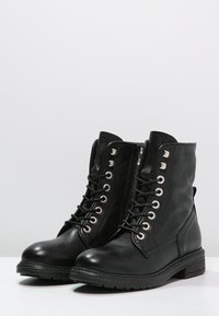 Bottes hautes en cuir noir avec bout arrondi, laçage à l'avant, œillets métalliques et fermeture éclair latérale. Surface texturée et petit talon empilé.