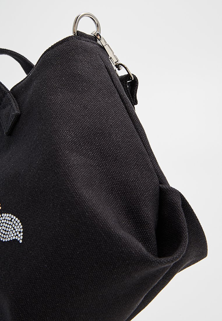 Sac en toile noir avec quincaillerie argentée, présentant une surface texturée et un design décoratif en strass. Forme compacte avec une fermeture sécurisée.