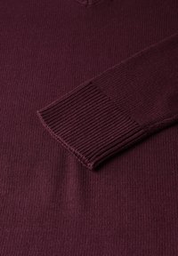Pull en tricot bordeaux avec un col en V, des poignets côtelés et une surface texturée, mettant en avant un tissu doux et chaud.
