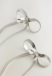 Silberne Ohrringe mit einem gedrehten, bandartigen Design, das eine geschwungene Schleife und eine zylindrische Rückseite aufweist. Glatte, metallische Textur.