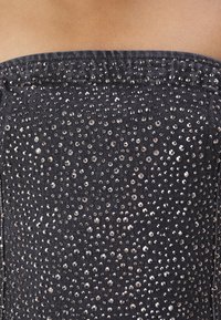 Svart denimmaterial med en figurnära, axelbandslös design, prydd med många silverpaljetter jämnt fördelade över tyget.