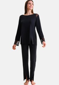 Zwart lounge-outfit met lange mouwen en splitten op de broek. De top heeft kanten accenten op de mouwen. Zachte, gladde stof.
