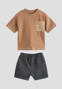 T-shirt en coton beige avec une poche à motif, associé à un short gris foncé doté d'un cordon de serrage et de poches latérales.