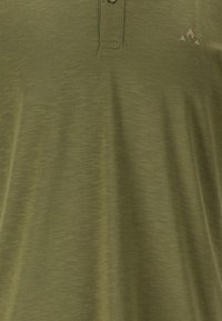 Olivgrön polo skjorta gjord av lättviktig tyg med en texturerad yta. Har en treknapplösning och en liten logotyp på bröstet.