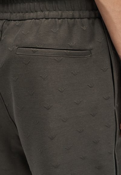 Κοντινή λήψη σκούρου γκρι παντελονιού με ελαστική μέση, πίσω τσέπη με σχίσιμο και διακριτικό ανάγλυφο επαναλαμβανόμενο μοτίβο λογότυπου.