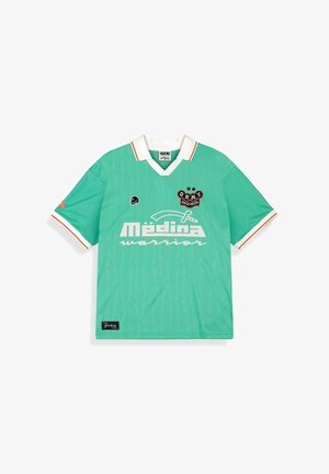 Zielona koszulka polo z krótkim rękawem, białym kołnierzem i mankietami, białą i pomarańczową lamówką oraz białym napisem "Médina warrior" z logo na przodzie.