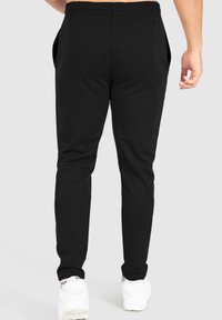 Schwarze Jogginghosen mit schmalem Schnitt, elastischem Bund und Seitentaschen, aus weichem Material. Getragen mit weißen Sneakers.