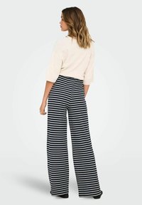 Spodnie typu wide-leg w granatowo-białe pionowe paski, z elastycznym pasem i miękkiego materiału. Modelka ma na sobie jasną bluzkę.