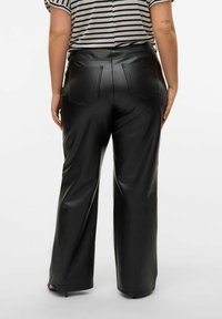 Pantaloni neri in finta pelle con un design a gamba larga, dotati di tasche posteriori e una texture liscia. Camicia a righe parzialmente visibile sopra.