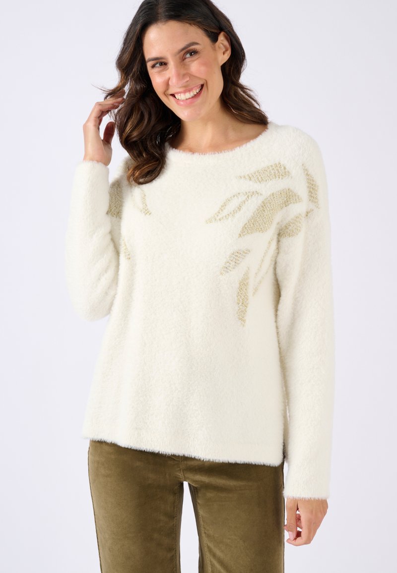 Suéter blanco esponjoso con cuello redondo y patrón de hojas doradas en el lado izquierdo, combinado con pantalones de textura verde oliva.