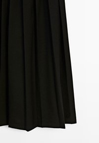 Černá skládací sukně visící přímo s viditelnými záhyby na bílém pozadí.