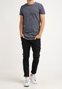 Men's casual outfit featuring a heathered dark blue T-shirt, black slim-fit jeans, and white sneakers with three strap closures.
