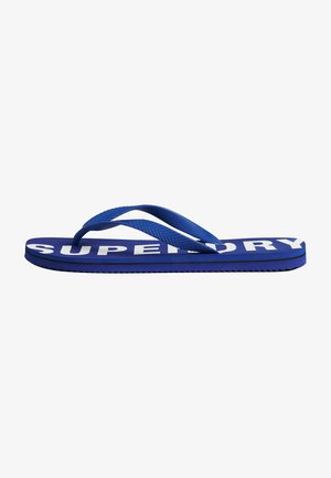 Blauer Gummilatschen mit einem strukturierten Riemen und großem weißen "SUPERDRY"-Logo auf der Fußbett. Besitzt eine gerippte Sohle für besseren Grip.