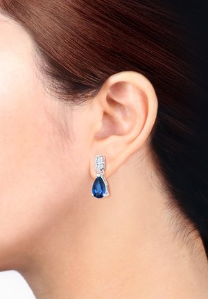 Silberne Tropfenohrringe mit einem großen blauen Stein und kleineren klaren Akzenten oben, die Eleganz und Kontrast im Design betonen.