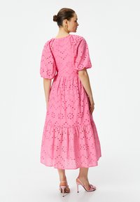 Roze katoenen jurk met pofmouwen, oogjesdetail en een gelaagd zoom. Doorzichtige accenten en een getailleerde taille verbeteren het ontwerp.