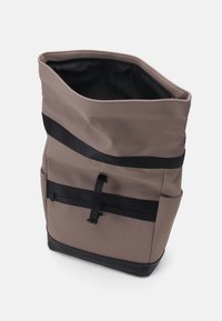 Borsa tote in tessuto grigio con dettagli neri, caratterizzata da una forma affusolata, spallacci regolabili e una chiusura superiore con cerniera. Dettaglio della tasca frontale visibile.