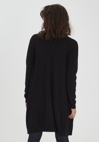 Lange zwarte cardigan van zacht gebreid materiaal, met een relaxte pasvorm, lange mouwen en een lengt tot halverwege de bovenbenen met zijsplitten.