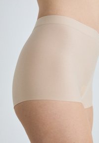 Slip beige senza cuciture in stile boyshort, con una texture liscia e un'ampia vita. Il tessuto sembra elastico e aderente.