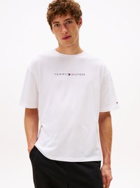 T-shirt bianco in cotone con collo giro, maniche corte e stampa di logo in blu navy e rosso sul petto. Design semplice e vestibilità rilassata.