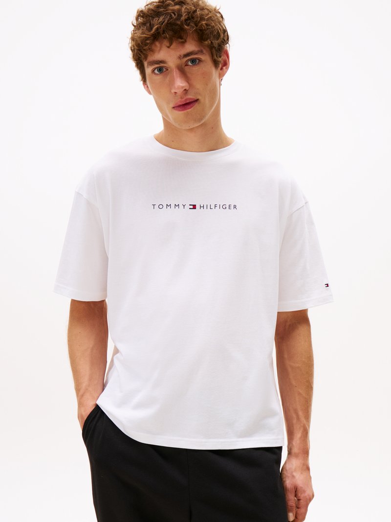 T-shirt bianco in cotone con collo giro, maniche corte e stampa di logo in blu navy e rosso sul petto. Design semplice e vestibilità rilassata.