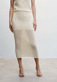 Robe en maille de couleur crème, avec un haut ajusté et une jupe mi-longue à texture ajourée. Associée à des sandales marron à brides.