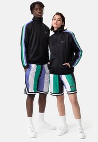 Juodas užtrauktukas sportinis švarkas su žaliais, mėlynais ir violetiniais dryžiais. Derantys daugiaspalviai šortai su vertikaliais dryžiais, juodu apvadu ir logotipu.