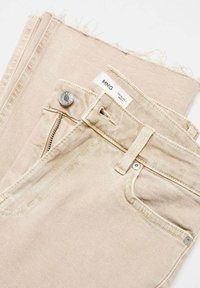 Beige denimfarkut, joissa on revitty helma, hopeinen nappikiinnitys ja vetoketju. Ominaisuuksiin kuuluu etutaskut ja ommeltu yksityiskohtia. Merkkilappu näkyvissä.