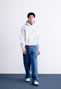 Lys grå hættetrøje med en frontlomme, parret med løstsittende blå denimjeans. Hvide sneakers fuldender looket. Minimalistisk design, afslappet pasform.