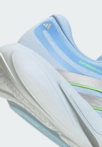 Light blue athletic shoe with textured mesh upper, silver accents, and green logo. Features a curved white midsole and rubber outsole details.