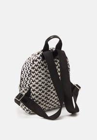 Ryggsäck med ett svart och vitt hjärtmotiv, tillverkad av tygmaterial, vadderad kropp och justerbara svarta remmar med ett handtag på toppen.