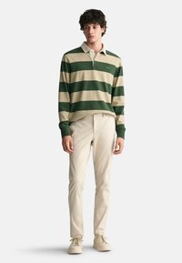 Green and beige striped long-sleeve polo shirt with a collar, paired with beige trousers and light-colored shoes. Smooth textures throughout.