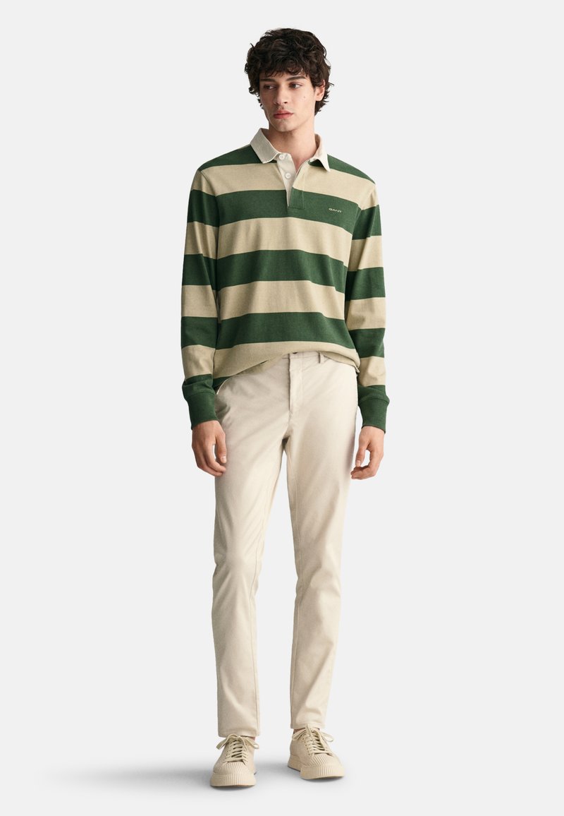 Green and beige striped long-sleeve polo shirt with a collar, paired with beige trousers and light-colored shoes. Smooth textures throughout.