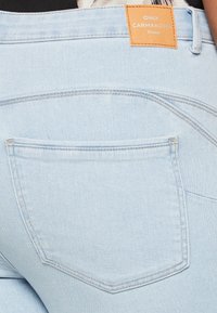 Ανοιχτό μπλε τζιν παντελόνι με καφέ ετικέτα που αναγράφει "ONLY CARMAKOMA" στη μέση. Διαθέτει μια πίσω τσέπη με ορατές λεπτομέρειες ραφής.