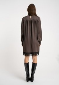 Brązowa satynowa sukienka z długimi rękawami, odkrytymi plecami z wycięciem i czarną koronkową lamówką u dołu. Połączona z czarnymi, wysokimi kozakami do kolan.