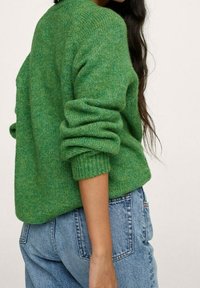 Grüner Strickpullover mit umgeschlagenen Bündchen und strukturierter Oberfläche. Dazu eine hoch taillierte blaue Jeans; Rückansicht gezeigt.