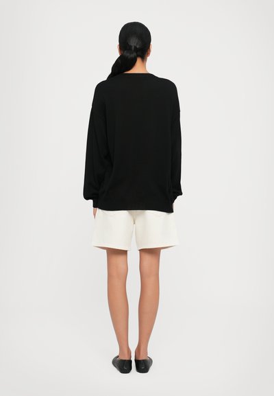 Schwarzer übergroßer Pullover, weiße Shorts und schwarze Ballerinas. Der Pullover hat lange Ärmel und eine lockere Passform, mit einem gerippten Halsausschnitt.