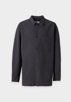Chemise noire à manches longues avec boutons, col et une poche poitrine unique, présentée sur un fond gris clair.