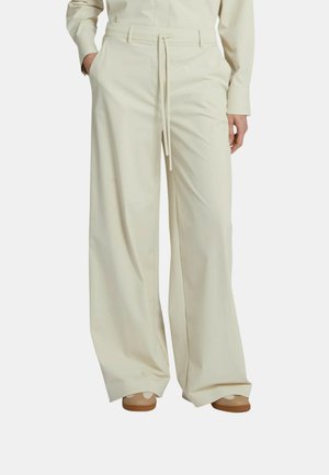 Pantaloni crema a gamba larga con tasche frontali e vita con coulisse, indossati con scarpe beige e camicia a maniche lunghe crema abbinata.