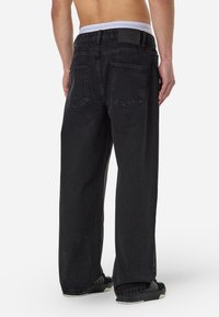 Sort denim jeans med løs pasform, der har en hvidtalje, to baglommer og en struktureret overflade. Designet til afslappet brug.