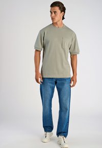 Kaki t-shirt med kort ärm och bröstficka, i kombination med blå raka jeans och vita sneakers. Slät tyg, avslappnad passform.