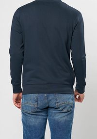 Mörkblå långärmad sweatshirt med ribbad textur, rund halsringning och enhetlig design, i kombination med blå denimjeans som har bakfickor.