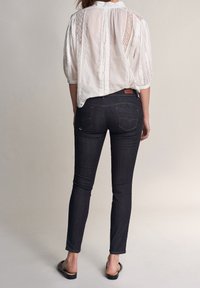 Vit, broderad blus med en plisserad rygg; mörka denim skinny jeans med lätt stretch och dubbla bakfickor; svarta sandaler.